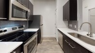 Located at 4150 S 300 E in Salt Lake City, Utah, this single-floor unit offers a thoughtfully designed open-concept layout with modern finishes throughout. The living area features durable hardwood-style flooring, a ceiling fan, and sliding door access, creating a bright and comfortable space. A peninsula with a white quartz countertop and undermount sink connects the living area to the kitchen, with a stylish pendant light overhead.

The galley-style kitchen is well-appointed with dark espresso cabinetry, grey subway tile backsplash, white quartz countertops, and a full suite of stainless steel appliances including a refrigerator, electric range, over-the-range microwave, and dishwasher. The layout maximizes efficiency while providing ample storage.

An arched doorway leads from the main living area to a dedicated hallway, which provides access to the bedroom and in-unit laundry. The bedroom is carpeted and benefits from natural light through a window fitted with blinds. The bathroom is finished in a clean, modern style with dark wood-tone cabinetry, a white vanity with an undermount sink, a large mirror, and a tub/shower combination with tile surround and brushed nickel fixtures.