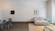 Located at 816 S Michigan Ave in Chicago's vibrant Grant Park corridor, this single-floor unit offers a thoughtfully designed layout that blends modern aesthetics with functional living. The open living area features warm hardwood-style flooring, high exposed ceilings with industrial undertones, and large windows that draw in natural light and frame urban views of the surrounding cityscape. Framed artwork and clean, neutral walls contribute to a calm, contemporary atmosphere.

The kitchen is appointed with sleek, modern cabinetry in a light wood finish, stainless steel appliances including a refrigerator, range, and microwave, and white countertops — offering an efficient and well-equipped cooking space.

Two bedrooms provide comfortable retreats. The primary bedroom features soaring ceilings with exposed structural elements, dark hardwood flooring, and direct access to an en-suite bathroom. The second bedroom is a cozier space with bright windows offering city views. Both rooms are styled with neutral tones and tasteful furnishings.

Two bathrooms mirror each other in design, each featuring floating wood-toned vanities with white countertops, undermount sinks, mirrored medicine cabinets, and tub-shower combinations — all finished in a clean, contemporary style. The overall ambiance of the unit is polished, urban, and inviting.
