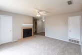 Located at 2102 W Loop 289 Frontage Rd in Lubbock, TX, this single-story unit offers a functional and straightforward layout across several distinct areas. The living room serves as the central gathering space, finished with plush carpet and anchored by a tile-surround fireplace with a white mantel — a practical focal point for cooler months. A ceiling fan with a light kit is mounted overhead, and a textured ceiling adds a classic touch throughout. The space flows into an additional carpeted room, also equipped with a ceiling fan, which can function as a dining area or secondary living space. The galley-style kitchen is lined with warm oak cabinetry, dark countertops, and black appliances including a refrigerator, range, and dishwasher, all set atop wood-look vinyl flooring that carries a clean, modern feel. A secondary kitchenette area with upper cabinetry and a sink adds extra utility. The bedroom is generously sized with carpet flooring, a ceiling fan, and a window that brings in natural light. The bathroom features a dark granite-style vanity with an undermount sink, oak cabinetry above, a tiled shower-tub combo, and wood-look vinyl flooring, completing this practical and comfortable space.