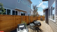 Unit B's backyard is a well-defined outdoor space enclosed by a warm-toned horizontal cedar privacy fence with metal post accents, providing a secluded retreat directly behind the multi-story building. The ground is finished with gravel covering, lending a low-maintenance and clean aesthetic to the area. A young tree anchors the space with natural greenery, complemented by ornamental plantings along the fence line that add texture and visual interest.

The backyard includes a dedicated lounge area outfitted with wicker seating, making it suitable for relaxed outdoor gatherings. A charcoal barrel grill on a stand adds outdoor cooking functionality to the space. The exterior of the building features a sliding glass door providing direct access between the interior and the backyard, enhancing the indoor-outdoor connection.

Beyond the private yard, the property offers access to a shared outdoor pool area, visible from the unit's exterior. The pool area is generously sized and surrounded by a concrete deck lined with lounge chairs and a separate spa, framed by mature trees. A covered entry with rustic wood-framed doors leads to the pool amenity. Together, the private backyard and shared pool area provide a comprehensive outdoor living experience suited to everyday use and entertaining.
