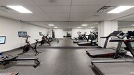 Located at 1475 Whites Rd in Pickering, Ontario, this fitness facility is a comprehensively outfitted exercise room designed to support a wide variety of workout routines. The space features a drop ceiling with recessed panel lighting that provides consistent, even illumination throughout, while durable rubber flooring offers both safety and comfort underfoot.

The strength training area is well-appointed with a cable machine, a weight bench, and a full dumbbell rack stocked with a wide range of weights. Large wall-to-wall mirrors in this zone visually expand the space and assist with form and technique. Adjacent to this, a dedicated cardio section houses multiple treadmills, stationary bikes — including a Peloton-style cycle — and a rowing machine, all equipped with individual monitors for performance tracking.

A separate boxing alcove provides a freestanding heavy bag station, offering a focused area for combat-style training. The main floor also includes a wall-mounted flat-screen television, a water fountain for easy hydration, and a sanitation station to promote cleanliness. Decorative bamboo plants add a touch of natural warmth to the otherwise sleek, modern aesthetic. The overall design is clean, functional, and well-organized, catering to a broad range of fitness goals in a purposeful and accessible environment.