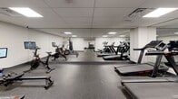 Located at 1475 Whites Rd in Pickering, Ontario, this fitness facility is a comprehensively outfitted exercise room designed to support a wide variety of workout routines. The space features a drop ceiling with recessed panel lighting that provides consistent, even illumination throughout, while durable rubber flooring offers both safety and comfort underfoot.

The strength training area is well-appointed with a cable machine, a weight bench, and a full dumbbell rack stocked with a wide range of weights. Large wall-to-wall mirrors in this zone visually expand the space and assist with form and technique. Adjacent to this, a dedicated cardio section houses multiple treadmills, stationary bikes — including a Peloton-style cycle — and a rowing machine, all equipped with individual monitors for performance tracking.

A separate boxing alcove provides a freestanding heavy bag station, offering a focused area for combat-style training. The main floor also includes a wall-mounted flat-screen television, a water fountain for easy hydration, and a sanitation station to promote cleanliness. Decorative bamboo plants add a touch of natural warmth to the otherwise sleek, modern aesthetic. The overall design is clean, functional, and well-organized, catering to a broad range of fitness goals in a purposeful and accessible environment.