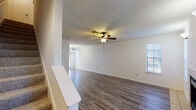 This two-story home offers a well-organized layout designed for comfortable everyday living. The main level centers around a spacious living area finished with durable hardwood-style flooring that flows throughout. A tile-surround fireplace serves as a focal point, adding warmth and character to the room, which is further enhanced by a ceiling fan with light kit and multiple windows that bring in natural light. An adjacent dining area connects seamlessly to the galley-style kitchen, which features warm honey-toned wood cabinetry, light countertops, a double-basin sink, and black appliances including a refrigerator and dishwasher. A door at the end of the kitchen provides convenient exterior access. The textured ceilings are consistent throughout the home, lending a classic residential aesthetic. Carpeted stairs lead to the upper level, where the bedrooms are finished with plush carpet and fitted with ceiling fans, offering a comfortable and quiet retreat. Windows with blinds in each bedroom allow for controlled natural light. The bathroom includes a vanity with warm wood cabinetry, a large mirror, and a tiled tub-shower combination. Overall, the home presents a functional and cohesive design with practical finishes across both floors.