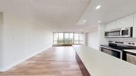 This well-appointed 3-bedroom, 2-bathroom residence is designed with a clean, modern aesthetic spread across a single floor. The open-concept living and kitchen area serves as the heart of the home, where large floor-to-ceiling windows flood the space with natural light and offer expansive outdoor views of surrounding greenery. Light hardwood flooring runs consistently throughout, enhancing the bright and airy atmosphere.

The kitchen is thoughtfully equipped with stainless steel appliances, including a range, built-in microwave, and refrigerator, complemented by sleek two-tone cabinetry and generous stone countertops. A raised kitchen bar seamlessly connects to the living area, making the layout ideal for everyday living.

Each of the three bedrooms is well-proportioned, with the primary bedroom offering notable space, mirrored sliding closet doors, and access to natural light. The living area and at least one bedroom feature sliding glass doors opening to a balcony, providing outdoor views.

The two bathrooms are finished in a clean, all-white palette, with one featuring a full soaker tub and tiled shower surround. Additional storage is provided by a dedicated closet near the entryway. Hallways connect the rooms efficiently, contributing to the unit's practical and functional layout throughout.