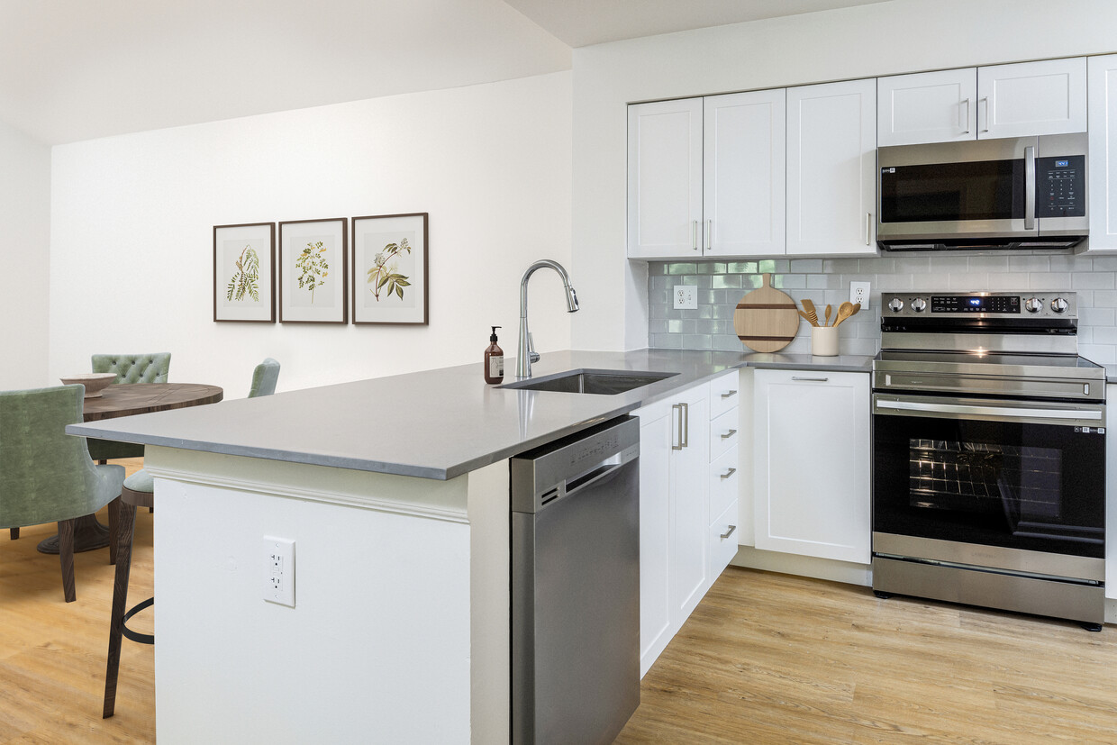 Renovated Package III kitchen with stainless steel appliances, grey quartz countertops (select homes), white cabinetry, light grey tile backsplash, and hard surface flooring - eaves West Windsor