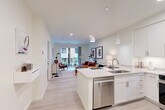 Located at 46 Soldiers Field Place in Boston, MA, this well-appointed one-bedroom, one-bathroom residence offers a thoughtfully designed open-concept layout. Light hardwood-style flooring flows throughout the main living area, connecting the kitchen, dining, and living spaces in a seamless, airy arrangement. The modern kitchen is outfitted with crisp white cabinetry, quartz countertops, stainless steel appliances—including a dishwasher, range, microwave, and refrigerator—and a peninsula island with bar seating, illuminated by sleek pendant lighting. The living area is bright and inviting, with access to a private balcony through full-height sliding glass doors that draw in natural light. The bedroom features a bold accent wall, plush carpeting, a large window with exterior views, and generous closet space. Two closets provide ample storage throughout the unit. The bathroom is finished with dark slate-style floor tiles, white subway tile in the walk-in glass shower, a white vanity with quartz countertop, and clean, contemporary fixtures. In-unit laundry adds everyday convenience, rounding out a residence that blends modern finishes with functional design in a compact yet comfortable footprint.