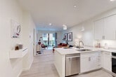 Located at 46 Soldiers Field Place in Boston, MA, this well-appointed one-bedroom, one-bathroom residence offers a thoughtfully designed open-concept layout. Light hardwood-style flooring flows throughout the main living area, connecting the kitchen, dining, and living spaces in a seamless, airy arrangement. The modern kitchen is outfitted with crisp white cabinetry, quartz countertops, stainless steel appliances—including a dishwasher, range, microwave, and refrigerator—and a peninsula island with bar seating, illuminated by sleek pendant lighting. The living area is bright and inviting, with access to a private balcony through full-height sliding glass doors that draw in natural light. The bedroom features a bold accent wall, plush carpeting, a large window with exterior views, and generous closet space. Two closets provide ample storage throughout the unit. The bathroom is finished with dark slate-style floor tiles, white subway tile in the walk-in glass shower, a white vanity with quartz countertop, and clean, contemporary fixtures. In-unit laundry adds everyday convenience, rounding out a residence that blends modern finishes with functional design in a compact yet comfortable footprint.