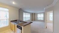 This single-floor residence is designed with a practical, open-concept layout that connects the living area and kitchen seamlessly. The living space is generously sized, featuring neutral beige carpeting, crown molding, and multiple large windows fitted with horizontal blinds that allow abundant natural light while offering views of the surrounding neighborhood.

The kitchen is functional and well-appointed, featuring light wood cabinetry, dark granite-style countertops, and stainless steel appliances including a refrigerator, range, and microwave. A peninsula with a double-basin sink separates the kitchen from the living area, creating an efficient workflow. Light tile flooring and recessed lighting complete the kitchen's practical design.

Two bathrooms serve the residence — one featuring a tub-shower combination with tiled surround and a single vanity, and another with a standalone shower, vanity, and tile flooring. Both maintain a clean, neutral aesthetic.

A dedicated laundry room houses a full-size top-loading washer and dryer, complemented by wire shelving above for added storage. A connecting hallway links the private areas of the home to the main living spaces, providing a clear and organized flow throughout.
