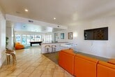 Located at 545 Sycamore Ln in Davis, CA, this single-story community clubhouse offers a generously sized, multi-functional layout designed for both recreation and productivity. The space is defined by a bright, modern aesthetic featuring crisp white walls, light tile flooring, and pops of bold orange, blue, and green throughout.

The main recreation area serves as the heart of the clubhouse, anchored by a full-size pool table beneath a pendant light fixture and flanked by large glass doors that flood the room with natural light and provide views of the outdoor courtyard. A foosball table and a wall-mounted flat-screen TV with vibrant orange leather seating create a comfortable, social lounge atmosphere. Colorful modular carpet tiles add energy and definition to the space.

A central lobby-style corridor connects the various zones, accented by tall potted plants, tile flooring, and casual seating including an oversized orange bean bag chair. A bar-height counter with stools offers a casual spot for socializing or working.

Dedicated workspaces include a glass-enclosed computer room equipped with desktop workstations and orange task chairs, as well as a separate study room featuring long wall-mounted desks, pendant lighting, and a distinctive textured blue brick accent wall. Together, these areas make this clubhouse a well-rounded community amenity.