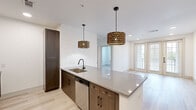Located at 321 W Ninth St in Dallas, TX, this single-story residence showcases a thoughtfully designed interior with modern finishes throughout. The open-concept kitchen serves as a central focal point, featuring a large island with a quartz countertop, dark wood cabinetry, stainless steel appliances including a refrigerator and dishwasher, and a matte black faucet at the undermount sink. Two decorative drum pendant lights with an ornate gold finish hang above the island, adding warmth to the space. Light wood-tone flooring runs throughout, complementing the clean white walls and creating a bright, cohesive aesthetic.

The living area receives natural light through large windows fitted with horizontal blinds. Bedrooms are finished with the same light flooring and white trim, including paneled doors with matte black hardware. The primary bathroom features a walk-in glass-enclosed shower alongside a dedicated vanity with quartz countertops and a herringbone accent wall. A secondary bathroom offers a soaking tub surrounded by large-format marble-look tile with matte black fixtures. A spacious walk-in closet provides built-in shelving and double hanging rods. The unit also includes a dedicated laundry area with a full-size side-by-side washer and dryer.