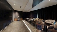 Located in East Brunswick, NJ, this upscale private screening room delivers an immersive cinematic experience within a thoughtfully designed single-floor layout. The space is anchored by a commanding large-format video wall display mounted against a deep charcoal accent wall, creating an immediate focal point upon entry. Recessed ceiling lighting provides controlled, subtle illumination, enhancing the room's moody, theater-like atmosphere.

The seating area is furnished with rows of generously sized, curved lounge chairs upholstered in rich textured fabric, arranged in a tiered configuration to ensure optimal sightlines to the screen. Sleek black side tables are positioned throughout for added convenience. Floor-level LED accent lighting traces the raised seating platform, lending a dramatic, modern edge to the interior.

Floor-to-ceiling dark drapery lines the walls, contributing to both acoustic quality and the room's refined aesthetic. The flooring transitions between stone-effect tile in the entry area and a patterned area rug beneath the seating, grounding the space with warmth and texture. A wood-and-stone credenza with built-in beverage refrigeration is tucked along one wall, offering a convenient amenity for guests. The overall design balances luxury and functionality, making this an exceptional venue for private screenings or exclusive gatherings.