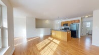 Located at 1175 Fort Hunter Road in Schenectady, NY, this one-bedroom, one-bathroom residence offers a practical and well-designed single-floor layout. The open-concept kitchen and living area serves as the heart of the home, featuring warm hardwood flooring that extends throughout the common spaces. The kitchen is equipped with a center island with a dark granite-style countertop and built-in sink, warm-toned wooden cabinetry, and black appliances including a refrigerator, electric range, and over-the-range microwave. A pendant light fixture above the island adds a focused accent to the space. The living area is bright and airy, bathed in natural light from large windows that frame views of the surrounding landscape. The bedroom is a comfortable retreat, fitted with plush carpeting, a spacious closet, and a window overlooking the wooded surroundings. The bathroom features a wooden vanity with a white countertop, a large wall mirror, tile flooring, and a window that brings in additional natural light. Clean white walls and neutral tones throughout the residence contribute to a cohesive and welcoming atmosphere, making this a well-appointed and functional home.