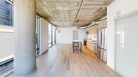 Located on Gordon Street in the heart of Hollywood, this one-bedroom, one-bathroom unit offers a distinctly modern industrial aesthetic across a generously sized single floor. The open-concept layout is immediately striking, defined by soaring exposed concrete ceilings with visible ductwork and structural columns that lend an authentic loft-like character throughout the living space.

Light-toned hardwood flooring runs continuously through the living and kitchen areas, creating a warm contrast to the raw concrete overhead. Floor-to-ceiling windows span multiple walls, flooding the interior with abundant natural light and framing impressive views of the Hollywood Hills and the surrounding cityscape, including a notable sightline to the Hollywood sign.

The kitchen is well-appointed with light wood cabinetry, stainless steel appliances including a refrigerator, range, and microwave, a clean tile backsplash, and an island workspace. A frosted glass sliding door adds a refined industrial touch near the kitchen entry.

The bedroom features large windows with roller shades, continuing the unit's emphasis on natural light. The bathroom is finished with large-format tile flooring, a tub-shower combination, a wood-toned vanity, and includes a stacked in-unit washer and dryer for added convenience.
