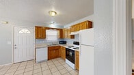 Located at 24480 Sesame Dr in Waynesville, Missouri, this single-floor unit offers a practical and well-organized layout designed for comfortable everyday living. The kitchen is a standout feature, outfitted with warm oak cabinetry providing ample storage, light-toned countertops, and tile flooring. It includes a full appliance suite — a white refrigerator, electric range with oven, dishwasher, and microwave — all neatly arranged in an efficient L-shaped configuration. A window above the sink brings in natural light, creating a bright and functional workspace. The open area adjacent to the kitchen flows seamlessly, also finished with tile flooring and neutral light-gray walls, offering a versatile living space. Bedrooms feature a mix of tile and plush carpeting underfoot. One bedroom is distinguished by a charming octagonal window alongside a standard window, allowing for generous natural light and a unique architectural touch. Soft gray walls and textured ceilings carry throughout the space, giving it a clean, cohesive look. The bathroom is finished with tile flooring, an oak vanity with under-sink storage, a large mirror with overhead lighting, and a separate toilet and shower area. Overall, the space presents a tidy, functional environment with consistent finishes throughout.