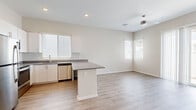 This well-designed 2-bedroom, 1-bathroom single-floor unit offers a clean, modern aesthetic throughout. The open-concept kitchen and living area serves as the heart of the space, featuring white cabinetry, dark countertops, a peninsula island ideal for casual dining or food prep, and a full suite of stainless steel appliances including a refrigerator, range, microwave, and dishwasher. Light wood-style vinyl flooring runs continuously throughout, tying the space together with a bright, cohesive feel. Multiple windows fitted with horizontal blinds allow natural light to pour in, while a ceiling fan in the living area adds comfort. A sliding glass door opens to an outdoor patio, extending the living space outside. Both bedrooms are well-proportioned and feature the same light flooring and neutral wall tones, with the second bedroom offering a window view of greenery. The shared bathroom includes a wide vanity with ample cabinet and drawer storage, dark countertops, and large mirrors. A dedicated laundry room houses a full-size washer and dryer, adding everyday convenience. A closet provides additional storage. The overall ambiance is clean, bright, and move-in ready.