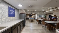 Located at 800 N Pennsylvania St in Denver, Colorado, this resident lounge is a well-appointed community amenity space designed for socializing and recreation. The layout is thoughtfully divided into distinct activity zones, all unified by exposed brick accent walls, light wood-look flooring, and recessed and pendant lighting that create a warm, urban-industrial atmosphere.

The lounge area features generous leather seating arranged around a rustic wooden coffee table, with a wall-mounted flat-screen TV serving as a focal point. Colorado-themed wall art and décor add a local character to the space. Adjacent to the lounge, a dedicated game room offers a full-size pool table, a shuffleboard table, and multiple wall-mounted TVs, making it an ideal space for friendly competition and entertainment.

A bar-height counter with industrial-style stools provides additional seating and a social hub within the game area. The community kitchen is sleekly finished with dark cabinetry, a light stone countertop, a mosaic tile backsplash, stainless steel appliances including a full-size refrigerator, and a deep utility sink — fully equipped for resident gatherings. Together, these amenities create a vibrant, functional communal space well-suited for the residents of this Denver community.