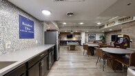 Located at 800 N Pennsylvania St in Denver, Colorado, this resident lounge is a well-appointed community amenity space designed for socializing and recreation. The layout is thoughtfully divided into distinct activity zones, all unified by exposed brick accent walls, light wood-look flooring, and recessed and pendant lighting that create a warm, urban-industrial atmosphere.

The lounge area features generous leather seating arranged around a rustic wooden coffee table, with a wall-mounted flat-screen TV serving as a focal point. Colorado-themed wall art and décor add a local character to the space. Adjacent to the lounge, a dedicated game room offers a full-size pool table, a shuffleboard table, and multiple wall-mounted TVs, making it an ideal space for friendly competition and entertainment.

A bar-height counter with industrial-style stools provides additional seating and a social hub within the game area. The community kitchen is sleekly finished with dark cabinetry, a light stone countertop, a mosaic tile backsplash, stainless steel appliances including a full-size refrigerator, and a deep utility sink — fully equipped for resident gatherings. Together, these amenities create a vibrant, functional communal space well-suited for the residents of this Denver community.