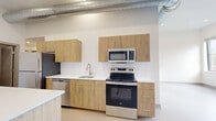 Located at 547 River St in Troy, NY, this thoughtfully designed one-bedroom, one-bathroom unit blends modern finishes with industrial character across a single floor. The open-concept living, dining, and kitchen area serves as the heart of the space, anchored by a striking kitchen featuring light wood cabinetry, white quartz countertops, a central island, and a full suite of stainless steel appliances including a refrigerator, range, microwave, and dishwasher. Exposed ductwork runs along the soaring ceilings, adding an authentic loft-style aesthetic, while white-painted brick accent walls lend warmth and texture throughout. Pendant lighting over the kitchen island and recessed fixtures provide layered illumination. A dedicated den offers flexible use as a home office or secondary lounge area. The bedroom is a calm, carpeted retreat with painted brick detailing. The bathroom is clean and contemporary, with a wood-toned vanity and ample built-in storage. A separate laundry area and closet add everyday convenience. The overall palette of whites, naturals, and warm woods creates a cohesive, inviting ambiance suited to modern living.