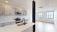 Located on the 11th floor at 933 McGee St in Kansas City, MO, this one-bedroom, two-bathroom unit offers a well-designed layout with modern finishes throughout. Warm hardwood-style flooring flows seamlessly across the entire space, complementing the clean white walls and creating a bright, cohesive aesthetic.

The open-concept kitchen and living area serves as the heart of the unit, featuring gray shaker-style cabinetry, white countertops, a classic subway tile backsplash, and stainless steel appliances including a range and microwave. A peninsula with an undermount sink and matte black faucet provides additional prep space and casual seating. A distinctive exposed structural column adds an industrial character to the space.

The bedroom is filled with natural light from large black-framed grid windows that frame elevated views of the Kansas City skyline and surrounding cityscape, giving the room an airy, open feel.

The bathroom is finished to a high standard, featuring a gray vanity with white countertop, matte black hardware, and a glass-enclosed walk-in shower clad in white subway tile with matching black trim accents. The unit also includes a dedicated closet for additional storage. Recessed lighting throughout adds a polished, contemporary touch to every room.