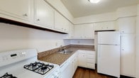 Located at 1414-1422 SOM Center Rd in Mayfield Heights, Ohio, this single-floor unit offers a well-organized layout designed for comfortable, everyday living. The kitchen is efficiently arranged in an L-shaped configuration, featuring white cabinetry with ample upper and lower storage, granite-look countertops, hardwood-style flooring, and a full suite of white appliances including a gas range, dishwasher, and refrigerator. The kitchen opens directly into the adjacent living area, creating a connected and functional flow throughout the space. The living room is generously proportioned, finished with plush neutral carpeting and fitted with a ceiling fan and light fixture. A sliding glass door leads to a private balcony that offers expansive elevated views of the surrounding Mayfield Heights area, allowing natural light to fill the room. Additional bedrooms are carpeted and bright, each featuring large windows with outdoor views and closet space. A carpeted hallway connects the private quarters, leading to a full bathroom appointed with white tile surround, a soaking tub and shower, wood-style flooring, a granite-look vanity countertop, and a large mirror. The overall aesthetic is clean, neutral, and move-in ready, providing a comfortable and practical living environment.