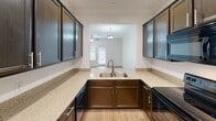 Located on Steiner Ranch Boulevard in Austin, Texas, this two-story residence offers a well-designed layout that balances functionality and comfort across both levels. The main floor features light hardwood-style flooring that flows throughout the open living areas, complemented by crown molding and recessed lighting that add a clean, refined finish to the space. A ceiling fan enhances the airy feel of the living room, which is bathed in natural light from blinds-covered windows.

The kitchen is a standout feature, offering rich dark cabinetry, granite-style countertops, a double-basin sink, and black appliances. A pass-through window connects the kitchen to the living area, creating an open and social atmosphere ideal for everyday living. Crown molding carries consistently throughout, maintaining a cohesive design language.

Upstairs, the carpeted bedrooms provide warmth and comfort, each accented with crown molding and ceiling fans. The primary bedroom connects to an en-suite bathroom featuring a soaking tub with tile surround, a separate glass-enclosed shower, a dark-cabinetry vanity with granite countertops, and a window for natural light. A secondary full bathroom includes a tub-shower combination with clean white tile finishes. A carpeted staircase with a warm wood handrail connects both floors seamlessly.