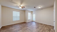 This single-story, 2-bedroom, 2-bathroom unit is thoughtfully laid out to maximize functionality within a comfortable footprint. The open-concept living and kitchen area serves as the heart of the space, where wood-style hard flooring extends throughout and a ceiling fan provides overhead lighting and airflow. Multiple windows fitted with blinds allow natural light to fill the room, while a private entry door connects directly to the living area.

The kitchen is equipped with warm-toned wood cabinetry, light granite-style countertops, white appliances including a range, microwave, and refrigerator, and a double-basin sink. A peninsula counter separates the kitchen from the living area, offering additional workspace and a casual seating option. A dedicated utility room is accessible from the kitchen.

The primary bedroom offers a comfortable amount of space with plush carpeting, a natural window, a walk-in closet, and a private en-suite bathroom featuring a walk-in shower with grab bars and wood-style flooring. The second bedroom is also carpeted with a window providing natural light, supported by its own closet. The second bathroom mirrors the clean, neutral finishes found throughout the unit.