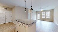 This thoughtfully designed single-floor residence offers a seamless blend of modern style and practical living. The open-concept kitchen and living area serves as the heart of the home, anchored by a central island with a sleek stone countertop and dramatic pendant lighting overhead. The kitchen is fully equipped with stainless steel appliances, ample white cabinetry, a classic subway tile backsplash, and recessed lighting — creating a clean, contemporary aesthetic. Light wood-style flooring flows throughout the main living areas, complementing the neutral warm-beige palette on the walls.

The living area benefits from a ceiling fan and a bright exterior-facing door that invites natural light deep into the space. The bedroom is a comfortable retreat featuring plush carpet, dual windows overlooking the surrounding neighborhood, and generous wall space. A dedicated closet provides practical storage. The bathroom is finished with wood-look tile flooring, a wide vanity with a white countertop, and a full soaking tub with large-format tile surround. Clean lines, neutral tones, and consistent modern finishes unify the entire residence into a cohesive, inviting living environment.
