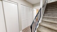 This two-story home in Indianapolis, Indiana offers a practical and well-appointed layout spread across two floors. The main level features a living room anchored by a wood-burning fireplace and light-toned luxury vinyl plank flooring that flows throughout. A dedicated dining room with chair rail molding sits adjacent, offering a view through to the living area and access toward a sliding glass door that opens to the backyard. The kitchen is thoughtfully updated with white cabinetry, marble-look countertops, a classic white subway tile backsplash, a double basin sink, and black appliances. A hallway on the main level provides built-in storage with large louvered bi-fold closet doors. Upstairs, three bedrooms offer comfortable retreats, each with plush carpeting and natural light from well-placed windows. The generously sized primary bedroom includes a closet with sliding panel doors. The three bathrooms are clean and functional, featuring wood-look flooring, white vanities with dark hardware accents, framed mirrors, and tiled tub-shower combinations. A carpeted staircase with a black metal railing connects the two floors. Textured ceilings and neutral warm-gray walls are consistent throughout, lending the home a cohesive and move-in-ready character.
