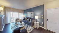 This thoughtfully designed single-floor residence offers a cohesive layout that balances comfort and functionality. The open-concept living area is a standout, featuring rich dark hardwood flooring, a bold blue accent wall, and large windows that invite an abundance of natural light. A tile-surround fireplace anchors one end of the living space, adding warmth and character. Adjacent to the living area, the dining room is highlighted by an elegant chandelier, a large decorative mirror, and direct sightlines into the kitchen, creating a seamless flow ideal for entertaining. The kitchen is well-equipped with warm wood cabinetry, dark granite countertops, a grey tile backsplash, and stainless steel appliances including a range, built-in microwave, and dishwasher. The primary bedroom features plush carpeting, a soothing sage green accent wall, and generous natural light from a large window. The second bedroom mirrors this comfort with a blue accent wall and bright window exposure. The primary bathroom offers a dual-sink vanity, dark wood cabinetry, a glass-enclosed walk-in shower, and direct access to a walk-in closet. A secondary full bathroom provides a single-sink vanity with matching cabinetry. Dark hardwood flooring flows throughout the main living areas, unifying the overall aesthetic of the space.