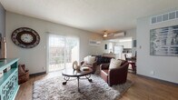 This single-floor residence offers a thoughtfully designed layout that balances comfort and functionality across its key living spaces. The living room serves as the heart of the home, featuring warm wood-style flooring, a ceiling fan, and a wall-mounted mini-split air conditioning unit. A large sliding glass door floods the space with natural light and opens to an outdoor patio, while a neutral color palette with a bold slate-gray accent wall adds visual depth and character. The kitchen is efficiently laid out with ample white cabinetry extending to the ceiling, light granite-style countertops, and white appliances including a refrigerator, electric range, dishwasher, and microwave — all set over matching wood-style flooring. The bedroom is a serene retreat, highlighted by a striking deep-blue accent wall, plush carpeting, a generous window with outdoor views, a walk-in closet, and its own wall-mounted air conditioning unit. The bathroom is clean and functional, featuring a vanity with countertop storage, a shower-tub combo with curtain, and wood-style flooring that ties into the rest of the home. Together, these spaces create a cohesive, comfortable living environment with a warm and inviting ambiance.