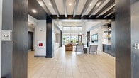 The Seasons at North Aurora Clubhouse at 1780 W Orchard Rd is a thoughtfully designed community facility offering a comprehensive range of amenities across a generously sized single-floor layout. The entrance welcomes visitors into a grand open lobby distinguished by striking dark exposed beam ceilings, bold structural columns, and large-format light tile flooring. Expansive windows flood the space with natural light, creating an open and airy atmosphere throughout.

The living and lounge area serves as a central gathering point, anchored by a dramatic floor-to-ceiling white stacked-stone fireplace and a built-in media wall. Modern, sculptural furnishings and colorful area rugs add warmth and personality to the space. Adjacent, a well-appointed kitchen features light wood cabinetry, a large white quartz island, stainless steel appliances, and pendant lighting, complemented by a snack and refreshment station with a glass-door beverage cooler.

The dining room offers a large communal table with direct access to an outdoor patio and pool area through floor-to-ceiling sliding glass doors — ideal for events and gatherings. The fitness center is fully equipped with strength machines, free weights, exercise balls, and wall-to-wall mirrors. A glass-enclosed leasing office completes the professional and welcoming atmosphere of this exceptional clubhouse.