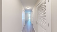 This thoughtfully designed one-bedroom, one-bathroom residence offers a clean, modern aesthetic throughout its efficiently organized single-floor layout. Light wood-tone flooring runs continuously through the main living areas and hallways, complementing the crisp white walls and trim that define the interior palette.

The open-concept kitchen and living area serves as the centerpiece of the unit. The kitchen is outfitted with light wood cabinetry, a white quartz waterfall island with an undermount sink, a subway tile backsplash, stainless steel appliances including a gas range and full-size refrigerator, and pendant lighting. Floor-to-ceiling windows flood the space with natural light and frame sweeping urban skyline views.

The living area continues the floor-to-ceiling window theme, offering expansive city views and a bright, airy atmosphere. The bedroom is a well-proportioned retreat featuring large sliding windows with city views and built-in closet storage with sleek, handle-minimalist doors.

The bathroom presents a clean, spa-like design with large-format tile flooring, a warm wood vanity with white countertop, an illuminated mirror, and ample space. Two hallways connect the rooms efficiently, with a dedicated entrance that provides a proper transition into the unit. Overall, the space reflects a contemporary urban design sensibility with high-quality finishes throughout.