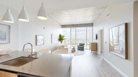 Located in the heart of Nashville at 805 Church Street, this modern one-bedroom, one-bathroom high-rise residence offers a refined urban living experience defined by clean lines, quality finishes, and breathtaking city views. The open-concept kitchen and living area serves as the heart of the home, where floor-to-ceiling windows flood the space with natural light and frame dramatic panoramic views of the Nashville skyline. The kitchen is appointed with stainless steel appliances, sleek cabinetry, a dark stone countertop island with bar seating, and pendant lighting overhead. Light hardwood flooring flows throughout, complementing the modern, neutral palette. Exposed concrete ceiling elements add an industrial character that contrasts beautifully with the bright, airy atmosphere. The bedroom continues the floor-to-ceiling window theme, offering sweeping views of the downtown skyline as a serene backdrop. Two closets and a dedicated laundry area provide practical storage solutions. The bathroom features a clean, contemporary design with a stone-topped vanity, an illuminated mirror, and large-format tile flooring. The welcoming entrance leads smoothly into the open living spaces, making the layout feel efficient and connected throughout.