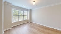 Located at Renaissance Park in Cary, NC, this two-story residence offers 2 bedrooms and 3 bathrooms thoughtfully distributed across two well-proportioned floors. The main level features an open-concept kitchen and living room filled with natural light from large windows. The kitchen is a standout, showcasing soft blue raised-panel cabinetry, stainless steel appliances including a range, microwave, and refrigerator, a white countertop island with a sink, pendant lighting, track lighting, and crown molding. Light wood-style flooring flows throughout the main living areas, adding warmth and continuity. The spacious living room opens to a private balcony through French doors with transom windows, offering pleasant views of the surrounding tree canopy and the Cary skyline. A dedicated in-unit laundry room with full-size washer and dryer adds everyday convenience. The upper floor hosts both bedrooms, each featuring light hardwood-style floors and generous windows. The primary bedroom includes balcony access via French doors and a ceiling fan. The bathrooms are well-appointed; the primary bath features dual sinks with distinctive blue cabinetry, while a secondary bath offers a glass-enclosed walk-in shower with white tile surround. A hallway and closet complete the layout, providing ample storage throughout.