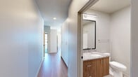Located on Cherry Street in the heart of downtown Green Bay, Wisconsin, this well-appointed 2-bedroom, 2-bathroom residence offers a modern living experience across a single thoughtfully designed floor. The open-concept kitchen and living area serves as the centerpiece of the home, featuring light wood-tone flooring, granite countertops, white upper cabinetry, and a tile backsplash. A large floor-to-ceiling window in the kitchen frames sweeping views of the surrounding cityscape, flooding the space with natural light. The living area extends this brightness with additional oversized black-framed windows and access to a balcony overlooking the neighborhood. Both bedrooms are generously proportioned, with large windows that capture elevated city views and plush carpeting underfoot. The primary bedroom includes a dedicated walk-in closet fitted with built-in shelving and hanging rods. The two bathrooms are finished with stone-look tile flooring and granite vanity tops; one features a walk-in shower with glass sliding doors, while the other offers a shower-tub combination. A dedicated in-unit laundry room with a front-load washer completes the practical layout. The overall design is clean and contemporary, with neutral tones creating a bright, cohesive atmosphere throughout.