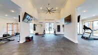 Located at 3415 US-41 in Warner Robins, Georgia, this single-story fitness facility offers a thoughtfully designed workout environment spread across a generously sized floor plan. The space is divided into two distinct zones, each tailored to specific training needs, connected by open passageways that promote a seamless flow throughout.

The main training area commands attention with soaring ceilings adorned with crown molding and an oversized multi-blade ceiling fan that anchors the space visually while ensuring air circulation. Dark gray tile flooring extends throughout, providing a durable, easy-to-maintain surface suited for high-intensity activity. Large sliding glass doors and expansive windows flood the area with natural light and offer views of the surrounding outdoor grounds. Wall-mounted flat-screen televisions and a bold "Hustle & Muscle" graphic add an energetic atmosphere. Equipment includes a heavy punching bag, cable machines, a rowing machine, and plyo boxes.

The secondary room features a mirrored wall, a full dumbbell rack with flat bench, medicine balls, and a barbell station, complemented by motivational "Harder. Better. Faster. Stronger." wall signage. A dedicated entry area with wood-plank flooring, wall-mounted cubbies, and bench seating provides a welcoming transition into the facility. Mini-split HVAC units ensure year-round climate control throughout both zones.