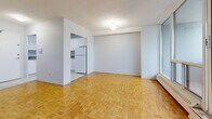 This well-organized 3-bedroom, 1-bathroom unit is spread across a single floor, offering a practical and comfortable layout. The spacious living room is a standout feature, boasting expansive floor-to-ceiling windows and sliding glass doors that open to a balcony, flooding the space with natural light and offering broad views of the surrounding cityscape. Classic parquet hardwood flooring runs throughout the living areas and all three bedrooms, adding warmth and a timeless aesthetic to the interior.

The primary bedroom is generously proportioned, featuring large sliding closet doors for ample storage. The two additional bedrooms are well-sized, each with parquet flooring; one includes a corner window that frames city views, while another features its own large sliding closet. A central hallway connects all rooms efficiently.

The kitchen is functional and neatly designed with white cabinetry, laminate countertops, and light tile flooring. It includes standard appliances and direct access to the unit's entrance. The bathroom features a full soaking tub with tile surround in neutral tones. A textured ceiling finish is present throughout the unit, consistent with the building's architectural character.