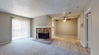 This single-story space offers a thoughtfully arranged layout that balances comfort and functionality. The main living area serves as the heart of the home, highlighted by a striking floor-to-ceiling stone fireplace with a raised hearth that anchors the room. Soft carpeting covers this area, while light wood-look flooring extends into the adjoining dining or secondary living zone, creating a natural visual transition between spaces. A ceiling fan overhead and vertical blinds flanking a large sliding glass door contribute to both comfort and natural light. The textured popcorn ceiling is consistent throughout.

The galley-style kitchen is well-equipped with ample white shaker cabinetry featuring matte black hardware, crisp white countertops, and black appliances including a range and refrigerator. A window above the counter brings in additional natural light. The bathroom features a clean white vanity with an integrated sink, a large mirror, and wood-look tile flooring that complements the kitchen. The bedroom is generously sized with plush carpeting, a ceiling fan with light fixture, a window with blinds, and access to a closet. Neutral warm-gray walls throughout the space provide a cohesive, move-in-ready aesthetic.