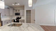 Located at 1000 Fazio Dr in Pinehurst, NC, this thoughtfully designed single-floor residence offers a clean, modern aesthetic throughout. The open-concept kitchen is a standout feature, showcasing granite countertops, gray shaker-style cabinetry with frosted glass upper panels, a classic subway tile backsplash, and a full suite of stainless steel appliances including a refrigerator, range, and built-in microwave. A peninsula with pendant lighting and an undermount sink creates a natural gathering point between the kitchen and living area. Warm hardwood-style flooring flows throughout the main living spaces, lending a cohesive and inviting feel. A dedicated pantry closet provides generous storage just off the kitchen. The hallway leads to well-proportioned bedrooms, including a primary suite with a spacious walk-in closet fitted with wire shelving. The primary bathroom features a sleek glass-enclosed walk-in shower, granite vanity, and hardwood-style flooring, while a secondary bathroom offers a full soaking tub with shower combination. A convenient in-unit laundry area with a full-size washer and dryer rounds out this functional and stylish residence.