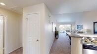 This thoughtfully designed single-floor residence offers a comfortable and functional layout that flows naturally from entry to living spaces. A welcoming hallway leads past a full bathroom and into the heart of the home, where the kitchen, dining, and living areas connect seamlessly. The kitchen is equipped with white cabinetry, granite-style countertops, stainless steel appliances including a gas range and built-in microwave, and a wraparound breakfast bar that opens to the main living area. The living room is highlighted by soaring vaulted ceilings that lend a sense of openness and airiness, with plush carpeting underfoot and a large sliding glass door that fills the space with natural light and provides access to an outdoor balcony or patio. The primary bedroom features vaulted ceilings, sliding glass door access to an outdoor area with exterior views, and soft carpeting throughout. A second bedroom offers a generous closet with sliding doors. Two full bathrooms serve the residence, each featuring a bathtub-shower combination and tile flooring. Throughout the home, neutral tones on the walls and ceilings create a bright, clean aesthetic, while textured surfaces and warm lighting add character and comfort to every room.
