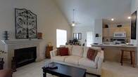 Located at 5885 Tuttle's Grove Blvd in Dublin, Ohio, this single-story home offers a well-designed layout with a bright and welcoming interior. The living room serves as the heart of the home, showcasing dramatic vaulted ceilings that lend a spacious, airy feel to the space. A ceiling fan is centrally positioned beneath the peak, ensuring comfort year-round. A tile-surround fireplace anchors one wall of the living room, adding warmth and a classic focal point to the area. Natural light flows freely through multiple windows, illuminating the neutral-toned walls and light carpeting throughout. The open-concept design creates a seamless transition from the living area into the kitchen, which features light wood cabinetry and a raised bar counter — ideal for casual dining or entertaining. The kitchen's layout offers both functionality and connectivity to the main living space. The overall ambiance of the home is calm and inviting, with a neutral color palette that provides a versatile backdrop. The combination of vaulted ceilings, natural light, and an open floor plan makes this Dublin property a comfortable and practical single-story residence.