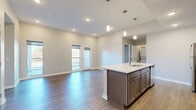 This single-floor residence offers three bedrooms, two bathrooms, and a well-designed layout that maximizes every square foot. The open-concept kitchen and living area serves as the heart of the home, anchored by a large central island with a light stone countertop, undermount sink, and pendant lighting above. Dark-toned cabinetry lines the kitchen walls, complemented by a full suite of stainless steel appliances including a refrigerator, range, and microwave. Wood-look flooring runs throughout the main living areas, enhancing the clean, contemporary aesthetic.

The living room connects directly to a private balcony through a glass-paneled door, allowing natural light to pour in and providing outdoor views. Two of the bedrooms feature plush carpeting and large windows with ceiling fans, while one bedroom benefits from direct outdoor access. The primary bedroom is a comfortable size and is served by a private bathroom with a wood-toned vanity and direct access to a well-organized walk-in closet featuring built-in shelving and hanging rods. An additional walk-in closet provides further storage throughout the home. Neutral wall tones and recessed lighting throughout contribute to a bright, modern ambiance.
