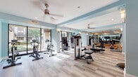 Located at 912 Innovation Way in Altamonte Springs, Florida, this fitness center offers a spacious, single-floor layout designed to support a wide range of workout routines. The interior is finished with light wood-style flooring and accented by soft blue and white walls, creating a bright and energizing atmosphere throughout the space.

Large floor-to-ceiling windows along one side of the main workout area flood the room with natural light and offer views of the surrounding outdoor greenery. Ceiling fans are positioned throughout to promote air circulation and comfort during exercise. Full-length mirrors line portions of the walls, enhancing the sense of openness and allowing users to monitor their form.

The facility is outfitted with an extensive selection of Freemotion-brand strength machines, cable systems, weight benches, and multi-purpose stations, catering to both targeted muscle training and full-body workouts. Cardio equipment, including stationary cycling bikes and treadmills, is also prominently featured. A dedicated area toward the rear of the space provides room for functional training, with medicine balls, a vertical knee raise station, and open floor space.

A hydration station and built-in cabinetry are available for convenience, and a glass-paneled partition wall separates zones within the facility. Recessed and wall-mounted lighting complements the natural light, ensuring the space remains well-lit throughout the day.