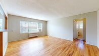 This well-organized one-bedroom, one-bathroom unit offers a practical and comfortable layout across a single floor. Warm hardwood flooring runs throughout the main living areas and bedroom, lending the space a cohesive and inviting character.

The living room is the largest area of the unit, featuring a textured ceiling, neutral walls, and a wide window fitted with blinds that allows natural light to filter in. A radiator beneath the window provides heating, complemented by a window-mounted air conditioning unit for year-round comfort.

The bedroom is a well-proportioned private retreat with its own window overlooking the surrounding exterior. A closet is accessible directly from the hallway, which also connects to the bathroom and the rest of the unit.

The kitchen is efficiently arranged with white cabinetry, granite-style laminate countertops, a gas range, a double-basin sink, and tile flooring. A window above the counter brings in natural light and adds to the room's functionality.

The bathroom includes a full bathtub with a tiled surround and a shower fixture, with tile flooring that transitions to the hardwood in the hallway. The hallway serves as a central connector between all rooms, providing an organized and navigable flow throughout the unit.