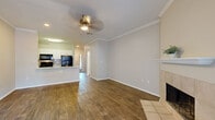 This two-story residence offers a thoughtfully designed layout spread across two floors of comfortable living space. The main level features an open-concept living room and kitchen, where warm hardwood-style flooring, crown molding, and a ceiling fan set an inviting tone. A tile-surround fireplace anchors the living area, adding a classic architectural detail. The kitchen is outfitted with white cabinetry, a peninsula with a white countertop and undermount sink, and black appliances including a refrigerator, range, and microwave. The lower level also includes a patio for outdoor enjoyment.

Upstairs, the second floor houses the three bedrooms, each finished with the same rich hardwood-style flooring and crown molding. The generously sized primary bedroom features a ceiling fan and direct access to a private balcony, filling the space with natural light. Each bedroom is complemented by its own closet for ample storage. The three bathrooms are well-appointed, with at least one featuring floor-to-ceiling large-format gray tile surrounding a soaking tub and shower combination. Two hallways and a staircase connect the floors seamlessly, creating a practical and cohesive flow throughout the entire home.