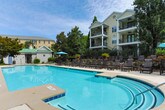 Located in the prestigious 30327 zip code of Atlanta, Georgia, this residential community blends classic architectural design with thoughtfully curated outdoor amenities. The exterior showcases traditional brick facades accented by white columns, arched windows, and decorative stonework, lending the property a timeless, upscale character.

The grounds are meticulously landscaped, featuring manicured hedges, seasonal blooms including hydrangeas, flowering crepe myrtles, and lush greenery that provides a verdant backdrop throughout the community. Charming hexagonal cobblestone-paved pathways wind through the property, lending a pedestrian-friendly, neighborhood feel reminiscent of a classic townscape.

A standout feature of this community is its expansive resort-style pool area. The sparkling turquoise pool is surrounded by a generous concrete deck lined with cushioned chaise lounges and additional seating, ideal for relaxation. A separate spa or wading area adjoins the main pool, and a dedicated pool house — painted in soft blue-gray tones with columned detailing — provides added convenience. The pool area is enclosed by a wrought iron fence and framed by a canopy of mature trees, offering both privacy and a serene natural atmosphere.

Overall, the community exudes a polished, comfortable ambiance that combines neighborhood charm with resort-quality outdoor living in one of Atlanta's most desirable areas.