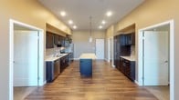 The Espresso floor plan is a well-appointed 2-bedroom, 2-bathroom single-story residence designed with both functionality and style in mind. The kitchen serves as a central highlight, featuring rich espresso-toned cabinetry that extends along multiple walls, light-toned granite countertops, and a full suite of stainless steel appliances including a range, microwave, refrigerator, and dishwasher. A central island with pendant lighting overhead adds additional prep space and anchors the kitchen's open layout. Warm hardwood-style flooring runs throughout the main living and kitchen areas, complementing the dark cabinetry for a cohesive aesthetic.

Both bathrooms mirror each other in design, each offering espresso-finish vanity cabinetry, white countertops, a large mirror with overhead lighting, a full tub-shower combination, and the same hardwood-style flooring for a consistent finish. The two bedrooms are comfortably sized, carpeted for warmth and comfort, and each features a window allowing natural light and outside views. A dedicated in-unit laundry room includes a full-size top-loading washer and dryer alongside wire shelving for additional storage. The overall ambiance is modern and practical, with a neutral color palette throughout.