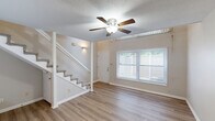 Located at 1841 Prospect Dr in Charlotte, NC, this two-story, one-bedroom, one-bathroom home offers a practical and comfortable layout spread across two floors. The main level features warm hardwood-style flooring throughout the living area, which is anchored by a ceiling fan and illuminated by natural light. A carpeted staircase with white railings leads to the upper level, where a pass-through counter hints at a kitchen tucked neatly beneath the staircase — a clever use of space. The upper level is home to the generously sized primary bedroom, which features soft carpeting, neutral wall tones, a ceiling fan with light fixture, and a textured ceiling. The bedroom connects directly to a closet and the full bathroom. The bathroom is clean and functional, equipped with a tub-shower combination, toilet, and vanity with countertop space. Consistent neutral tones and clean finishes run throughout the home, creating a cohesive and understated aesthetic. The exterior is surrounded by mature trees, offering a sense of privacy and natural character. This home provides a straightforward, well-organized living experience suitable for a single occupant or couple.