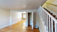 This three-floor home offers a practical and straightforward layout across its levels. The main living area is characterized by warm-toned hardwood floors that extend throughout, complemented by neutral light gray walls and clean white trim and baseboards. A white-painted staircase with open balusters provides access to the upper floor, positioned alongside a convenient storage closet on the main level. The living space flows into a dining area illuminated by a multi-light brass chandelier, adding a classic touch to the room.

The kitchen is equipped with medium-toned wood cabinetry, dark laminate countertops, and white appliances including a refrigerator, electric range, and over-the-range microwave. Stone-look tile flooring grounds the kitchen, which also features a built-in pantry closet for additional storage. A staircase is also accessible from the kitchen area, leading to additional levels.

The bathroom includes a tub and shower combination with white tile surround. The lower level consists of an unfinished basement with a painted concrete floor, exposed wood beam ceiling, utility systems including an HVAC unit, and a utility sink, providing functional storage and mechanical space.