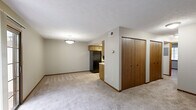 Located at 4880 Willow Glen Dr in Beech Grove, Indiana, this single-floor, one-bedroom, one-bathroom unit offers a well-organized and functional layout across a comfortable footprint. The kitchen is equipped with warm wood-toned cabinetry spanning both upper and lower sections, a double sink, light-toned countertops, and a built-in overhead light fixture. Black appliances, including a full-size refrigerator and dishwasher, complement the cabinetry, while light hardwood-style flooring adds a clean, practical finish to the space. The living area features soft wall-to-wall carpeting, neutral gray-toned walls, a textured ceiling, and a sliding glass patio door dressed with vertical blinds, allowing natural light to filter in and providing outdoor access. The bedroom is generously sized with plush carpeting, a textured ceiling, a built-in closet with a hanging rod, and a window with blinds that brings in additional natural light. The bathroom is straightforward and clean, featuring a full soaking tub with an overhead shower, chrome fixtures, and neutral-toned surround walls. Two hallways connect the rooms efficiently, contributing to the unit's cohesive and easy-to-navigate floor plan throughout.
